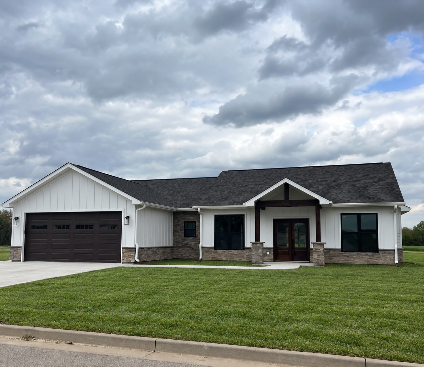 White home with dark roof, attached garage, stone accents, and a digitally added green lawn